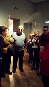 A klubtagok a múzeum egyik kiállítótermében hallgatják a tárlatvezetést