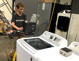 A képen a 14 éves fejlesztő látható, amint egy számítógépen a mosógépek digitális vezérlőihez programot készít