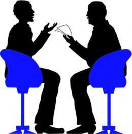 Két férfi fekete sziluettje, egyikük papírlapot tart kezében, közben beszélgetnek, a másik fél gesztikulál. Mindketten egy-egy erősen kontrasztos hatású kék forgószékben ülnek.