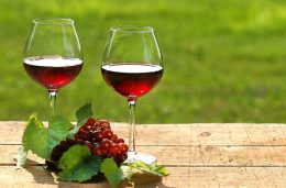 A képen két pohár vörösbor látható, egy fürt szőlővel, egy fából készült asztalon