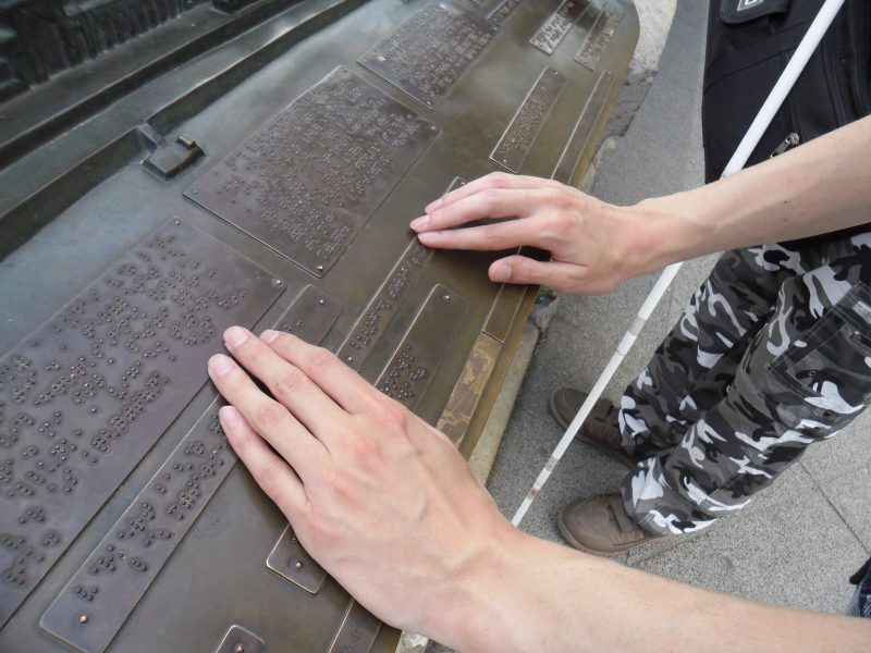 A korzó egyik Braille-felirata látható a képen amit a kispesti klub programján olvasnak ki a sétálók